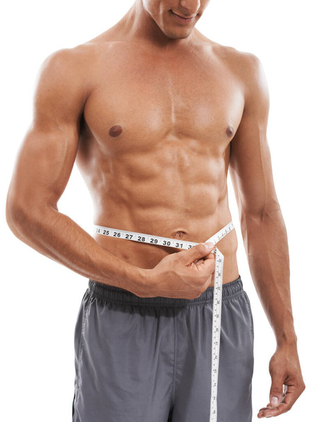 Measuring his rock hard abs. Cropped image of a muscular man measuring his torso against a white background - Foto, imagen