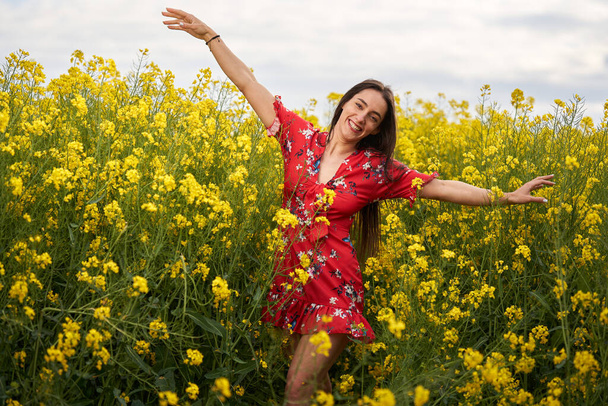 Portrait of a beautiful hispanic young woman in floral dress in a canola field at the end of the spring, in full bloom - Foto, Bild