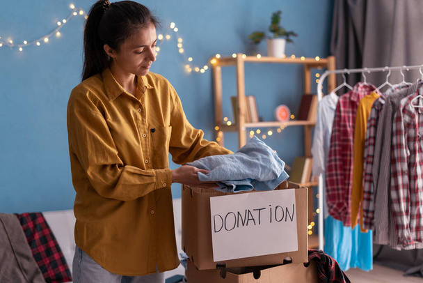 Concepto de donación. Mujer preparando su ropa vieja usada en una caja de donaciones. Copiar espacio - Foto, imagen