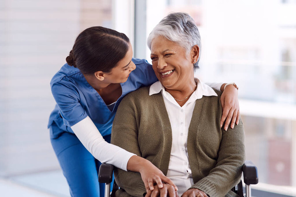 Υγεία, αναπηρία και μια νοσοκόμα που αγκαλιάζει μια ηλικιωμένη γυναίκα σε αναπηρικό καροτσάκι κατά τη διάρκεια επίσκεψης σε γηροκομείο. Ιατρικές, αγκαλιά και αστείο με ένα γέλιο γυναίκα γιατρός επαγγελματίας μιλάμε για ένα ανώτερο ειδικευόμενο. - Φωτογραφία, εικόνα