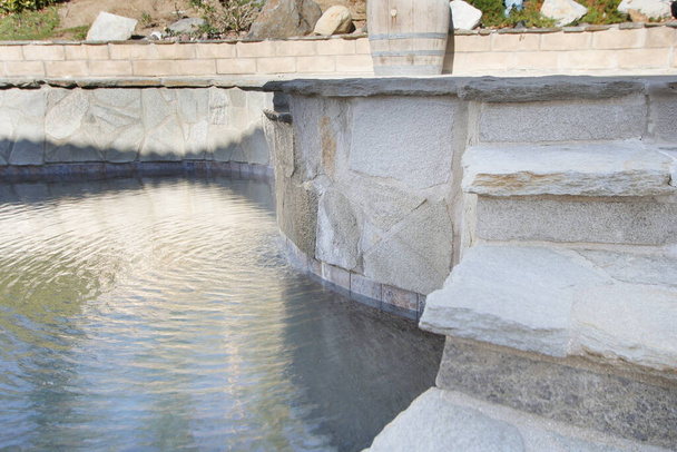 Uitzicht op een zwembad, voorzien van een stenen trap en mini waterval. - Foto, afbeelding