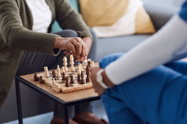 Χέρια, σκάκι μια νοσοκόμα με έναν ασθενή σε ένα γηροκομείο παίζοντας ένα παιχνίδι στρατηγικής κατά τη διάρκεια μιας επίσκεψης. Υγειονομική περίθαλψη, ιατρική ή ασφάλιση με επαγγελματία ιατρό και κάτοικο του σαλονιού μαζί. - Φωτογραφία, εικόνα
