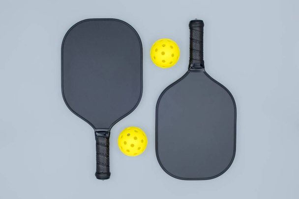 コピースペースとライトグレーの背景に2つのピックルボールパドルと2つの黄色のボールのトップビューの閉鎖 - 写真・画像