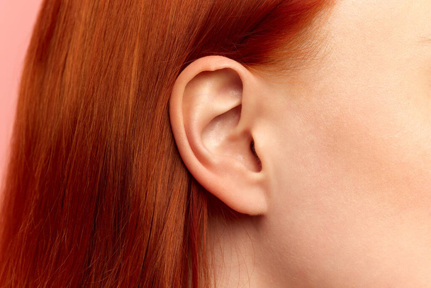 Cropped portrait with lower face, ear of young woman, girl with red hair and pink cheeks. Close up image. Model with well-kept, perfect skin. Ear piercing, beauty, treatment, cosmetology concept - Φωτογραφία, εικόνα