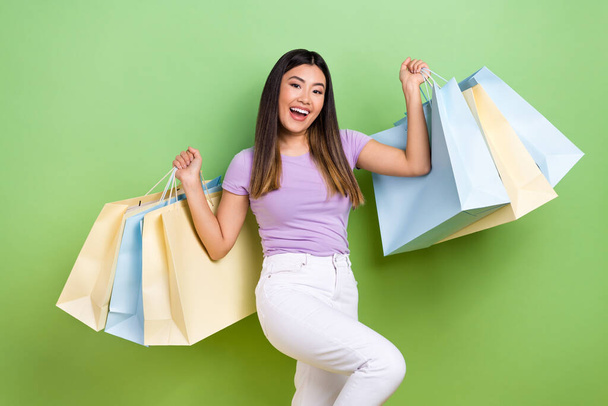 Photo of attractive vietnamese chinese young woman hold shopping packages dressed stylish violet clothes isolated on green color background. - Фото, изображение