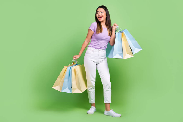 Full length body cadre of funky shopaholic girl hold packages look empty space new collection shoes isolated on green color background. - Fotografie, Obrázek