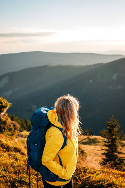 Woman with backpack hiking in mountains during sunset at autumn. Female hiker wearing yellow jacket - Photo, image