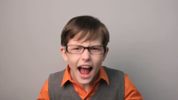 teenager boy swears row waving his arms opened his mouth in glasses on gray background - Footage, Video