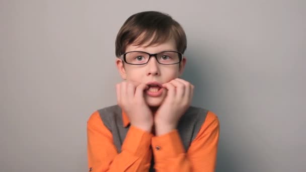 boy hands to his mouth fright shock glasses ten years on a gray background - Footage, Video
