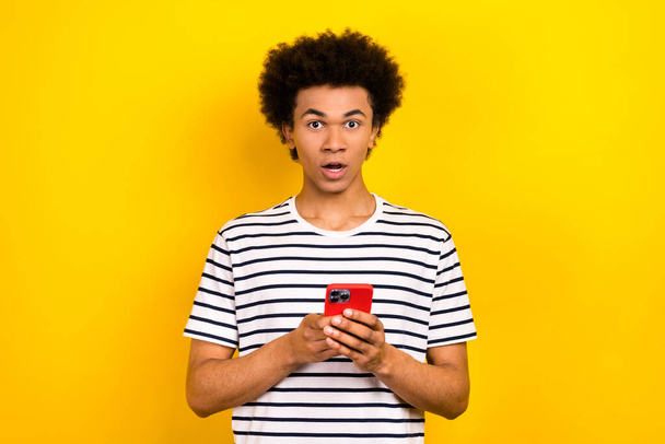 Photo of young funny guy wear t-shirt chevelure hair shocked his fast speed internet on device dont work isolated over yellow background. - 写真・画像