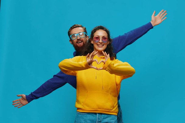 A woman and a man fun couple cranking and showing signs with their hands smiling cheerfully, on a blue background, The concept of a real relationship in a family. High quality photo - Photo, Image