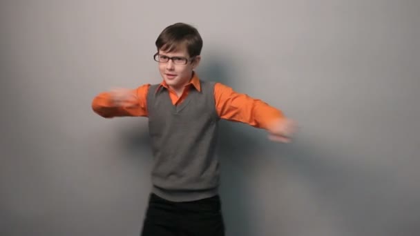 dospívající chlapec taneční zábavný mával rukama v brýlích deset let na šedém pozadí - Záběry, video