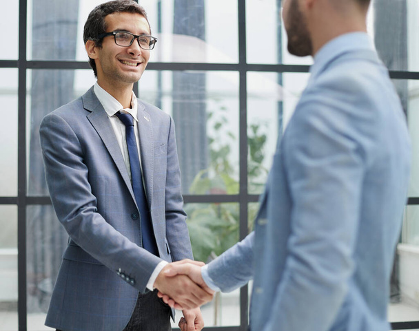 Businessmen shake hands, standing near a large office window - Foto, afbeelding