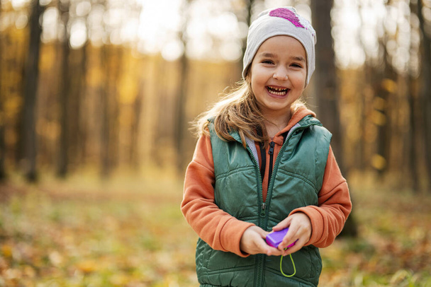 Autumn outdoor portrait of beautiful happy child girl in forest with toy photo camera. - Foto, Imagen