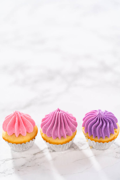 Freshly baked mini vanilla cupcakes with ombre pink buttercream frosting on a marble kitchen ocunter. - Photo, Image