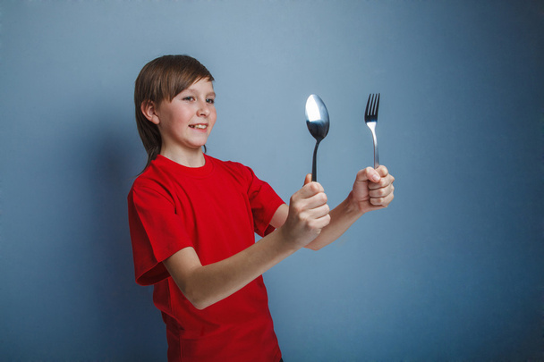 Teenager boy in red shirt twelve years holding  spoon and fork, - Photo, Image