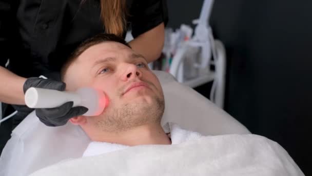 Une femme cosmétologue effectue la procédure de phonophorèse. Rajeunissement de la peau du visage pour les hommes. Un esthéticien effectue un lifting ultrasonique de la peau - Séquence, vidéo