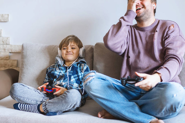 Отец и сын сидят на диване в гостиной и играют в видеоигры..  - Фото, изображение
