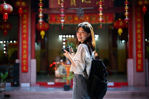 Attractive and smiling young Asian female tourist sightseeing and visiting a beautiful Chinese temple in Chiang Mai. Solo travel and historical sightseeing trip concept - Photo, Image