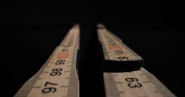 Medidores de madeira dobráveis que se estendem sobre a mesa escura no estúdio. Réguas de centímetros longos projetadas para medir o comprimento no fundo preto - Filmagem, Vídeo