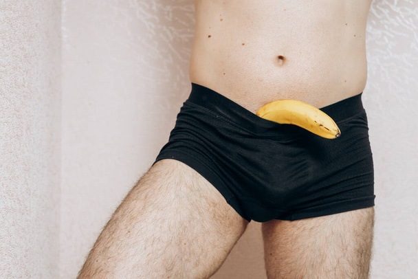 Un tipo sin ropa tiene un plátano perdido en la mano. Problema de erección, salud masculina - Foto, Imagen