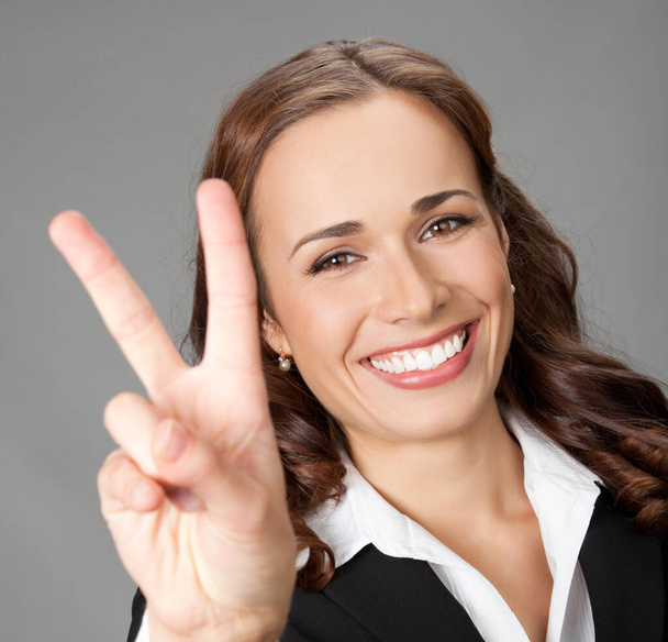 Happy smiling beautiful young business woman showing two fingers or victory gesture, over gray background - Foto, Imagem