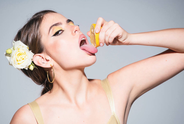 Pretty girl or sexy woman with stylish makeup on beautiful face squeezing juice from fresh orange citrus fruit, lick with tongue natural orange - Foto, imagen