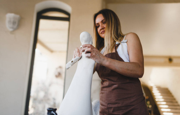una donna sta lavorando ad una statua nel suo laboratorio di ceramica. Lavori di ceramica. Creazione di prodotti argillosi. - Foto, immagini