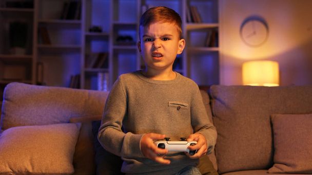 Portrait of a happy child playing a video game very hard with a joystick, looking intently at the camera at home. The concept of games and childhood - Foto, Imagen