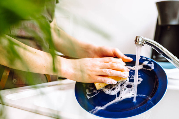 vrouw in het werk bruine koks schort, afwas met wasmiddel met spons, in de gootsteen in de keuken. concept schoonmaken, afwassen, werkvaatwasser - Foto, afbeelding