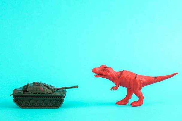 Zabawkowy czerwony dinozaur tyranozaur rex z wojskowym czołgiem na turkusowym tle. Minimalizm twórczy układ. Przerwać wojnę. - Zdjęcie, obraz