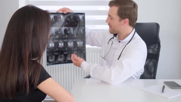 Un vertebrólogo muestra una imagen de rayos X de la columna vertebral a un paciente en el hospital. Mujer joven haciendo examen de columna vertebral en clínica de columna - Imágenes, Vídeo