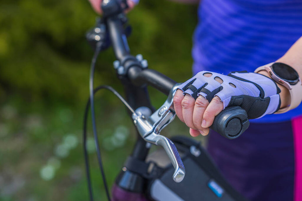 Vista della mano femminile in guanti sportivi e orologio da polso sul manubrio della bicicletta.  - Foto, immagini