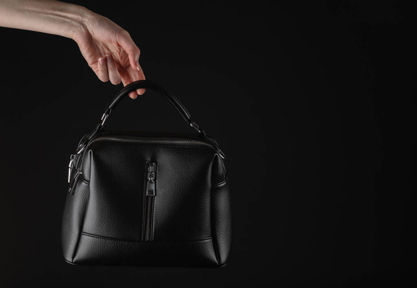 Female hand holding Black leather luxury handbag isolated on black background - 写真・画像