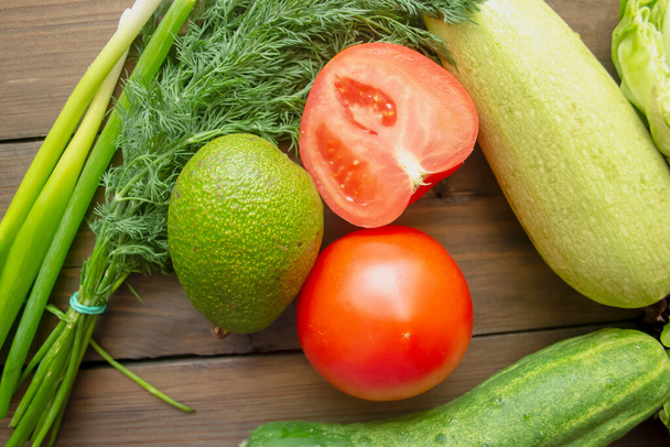 On a wooden table are healthy vegetables. green and red vegetables for health. Tomatoes, cabbage, zucchini, cucumbers and avocado for salad. - Fotó, kép