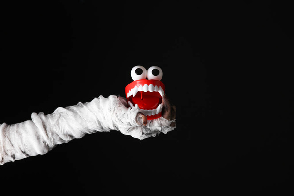 Mummy's hand wrapped in bandage holds monster joke jaw isolated on black background. Halloween concept - Photo, Image