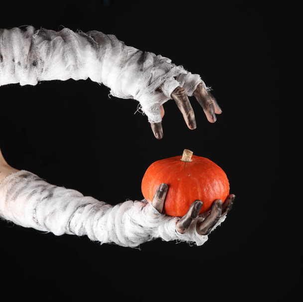 Mummy hands wrapped in bandage holds decorative pumpkin isolated on black background. Halloween concept - Photo, Image