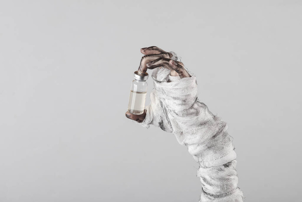 Mummy hand with vaccine bottle isolated on gray background. Halloween, gaming concept - Foto, Imagen