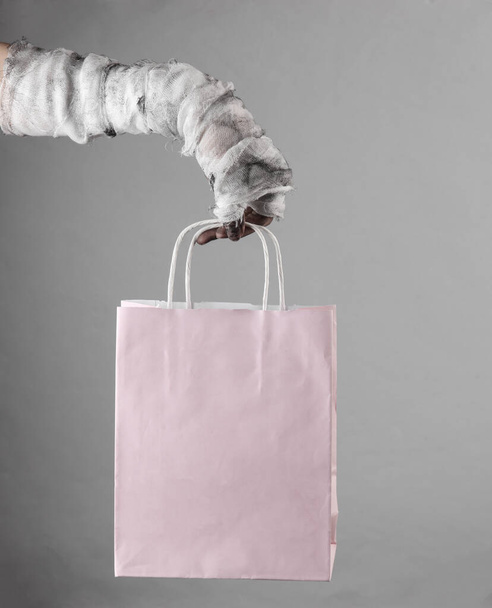 Mummy hand holding shopping bag isolated on gray background. Halloween concept - Photo, Image