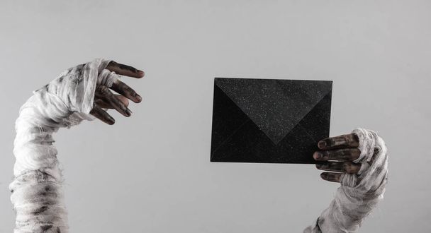 Mummy hand holding black envelope isolated on gray background. Halloween concept - Foto, afbeelding