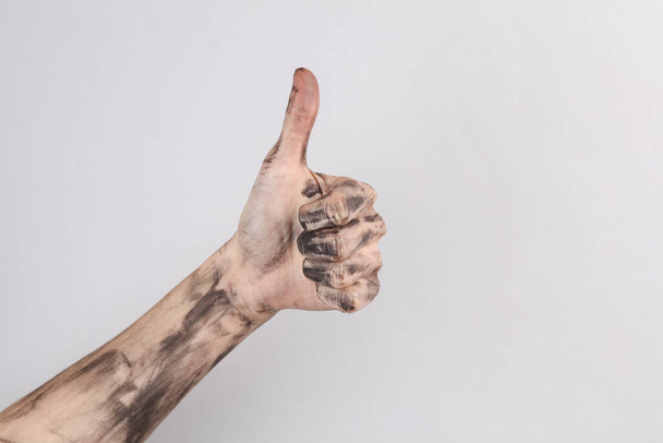 Hand in black paint or soot showing thumbs up on a gray background - Foto, afbeelding
