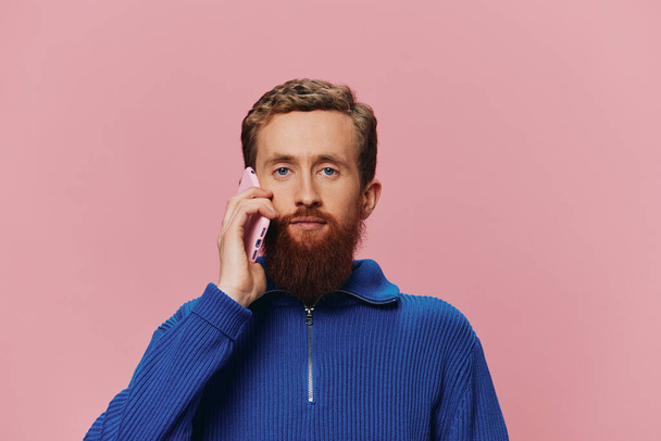 Portret van een man met een telefoon in zijn handen die ernaar kijkt en praat aan de telefoon, op een roze achtergrond. Communiceren online sociale media, levensstijl. Hoge kwaliteit foto - Foto, afbeelding