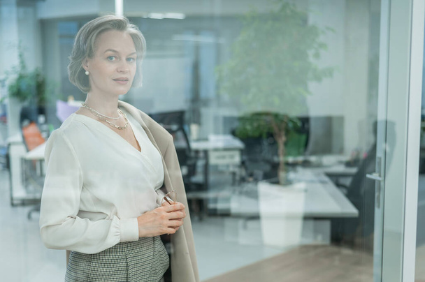 Portrét krásné šedovlasé bělošky v kanceláři stojící za skleněnou stěnou - Fotografie, Obrázek
