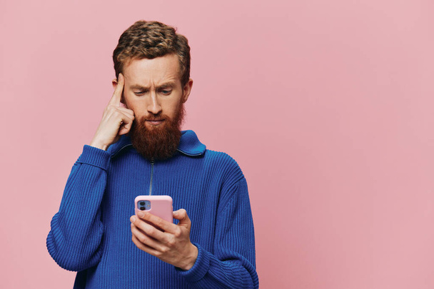 Elinde telefon olan bir adamın portresi. Pembe arka planda telefona bakıp konuşuyor. Çevrimiçi sosyal medya iletişimi, yaşam tarzı. Yüksek kalite fotoğraf - Fotoğraf, Görsel
