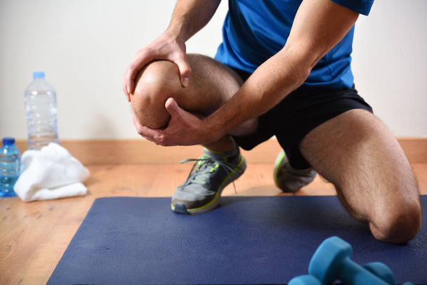 Detail of man doing sports with knee pain holding himself with his hand sitting on a mat. Front view. - Foto, imagen