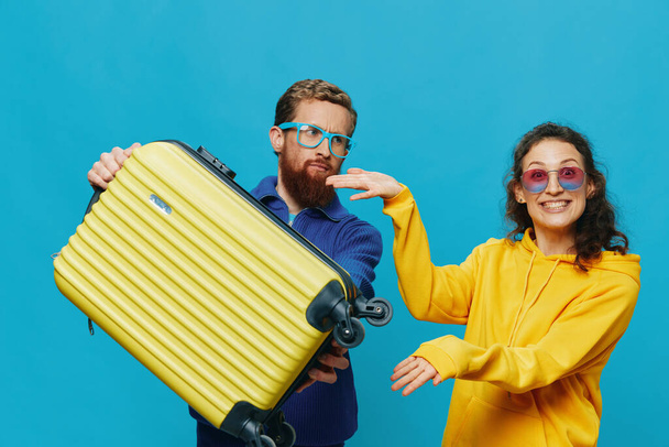 Mujer y hombre sonríen sentados en la maleta con una sonrisa amarilla en la maleta, sobre un fondo azul, empacando para el viaje, viaje de vacaciones en familia. Foto de alta calidad - Foto, imagen