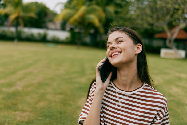 park kobieta student natura kaukaski telefon odkryty paski praca drzewo szczęśliwy człowiek uśmiechnięty połączenie lato przeglądanie komórka trawa palma blogger styl życia osoba - Zdjęcie, obraz