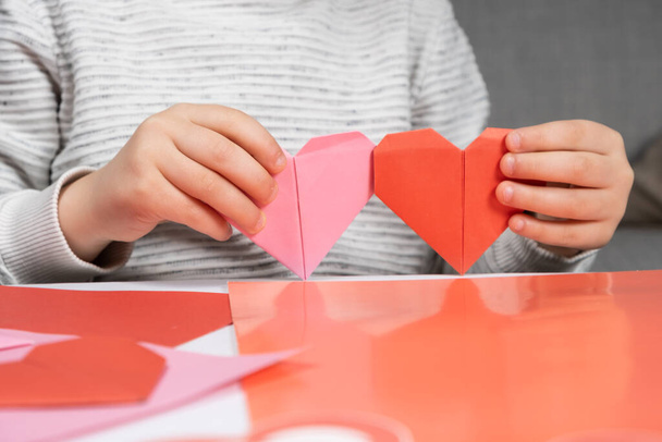 子供は紙から心を作り、手を閉じています。バレンタインデーの折り紙 - 写真・画像