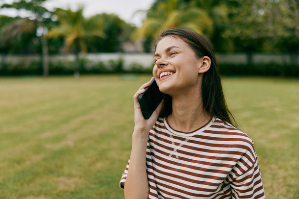 Блогер женщина образ жизни природа телефон здоровый человек парк дерево женщина трава говорить кавказский летний мобильный телефон улыбаясь пальма счастливый сезон девушка сотовый телефон красивая - Фото, изображение