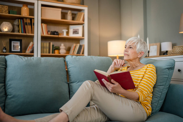 One woman mature senior caucasian female pensioner modern grandmother read book at home wear eyeglasses real person copy space - Foto, Bild